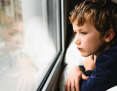 young boy looking sad staring out of a window
