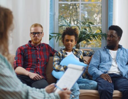 couple and their child sitting on sofa together in front of woman with clipboard