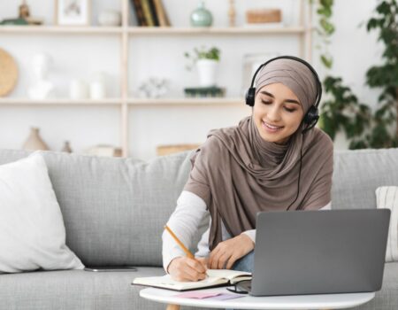 woman wearing headset sitting in front of laptop writing notes